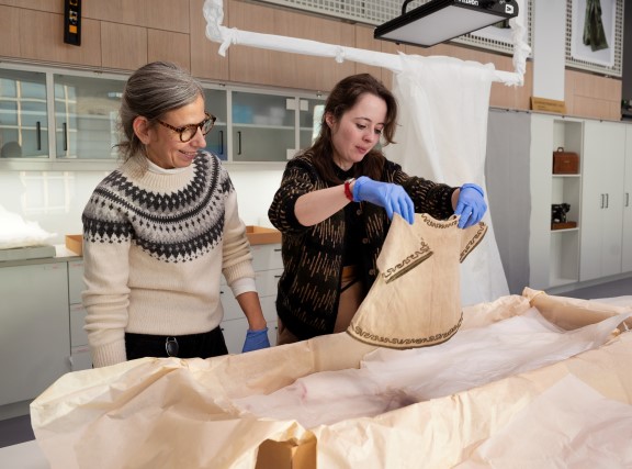 To kvinner pakker ut små klær fra esker på museum
