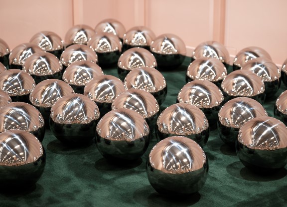 Mirror balls on a dark green carpet with pale pink walls in the background. 