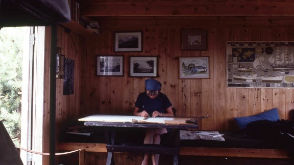 En dame sitter ved tegnebordet på en hytte